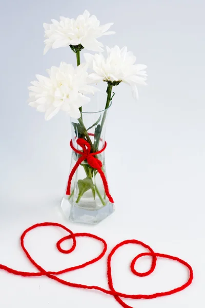 Fiori bianchi in un piccolo vaso di vetro con un fiocco rosso e due cuori da fili — Foto Stock