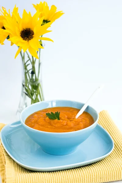 Zuppa di zucca in un piatto blu e un mazzo di fiori gialli — Foto Stock