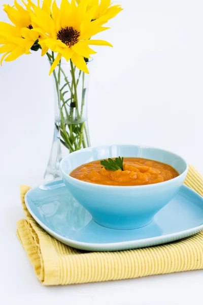 Pumpa soppa i en blå tallrik och en bukett med gula blommor — Stockfoto