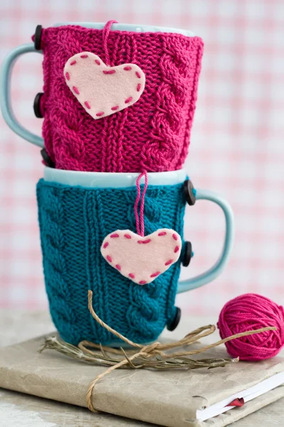 Две синие чашки в голубом и розовом свитере с войлочными сердцами на блокноте — стоковое фото