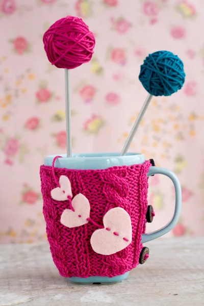 Голубая чашка в розовом свитере с войлочными сердечками с шариком пряжи — стоковое фото