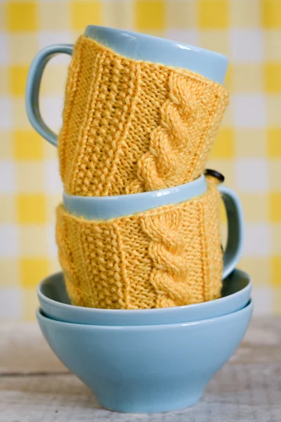 Dwa niebieskie filiżanki w żółty sweterek na tle tkaniny — Zdjęcie stockowe