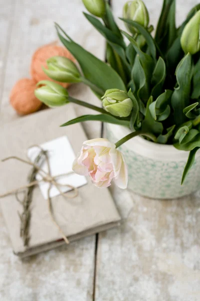 Bouquet of delicate pink tulips on a wooden background, vintage note pad and bright balls of yarn — Stock Photo, Image