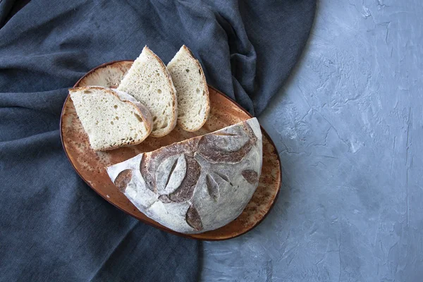 Vista superior de la mitad del pan y rebanadas en placa de cerámica sobre tela gris y fondo de madera horizontal — Foto de Stock