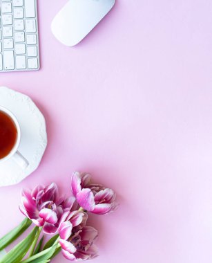Yarım fincan siyah çay, kablosuz beyaz klavye ve fare, pembe kopyalanmış üç pembe şakayık lalesi buketi.