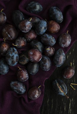 Koyu olgun sulu erikler, siyah ahşap bir zemin üzerinde uzanan mor bir masa örtüsünün üzerinde yatar..