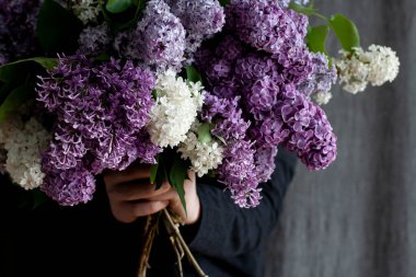 Genç yakışıklı adam elinde kocaman bir demet renkli leylak tutuyor.