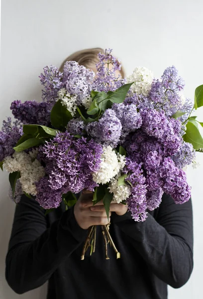 Genç yakışıklı adam yüzünü renkli kokulu leylakların arkasına saklar.