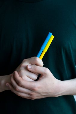 Rusya ile savaşta Ukrayna 'ya destek. Genç bir adam Ukrayna bayrağının bir sembolü olarak sarı ve mavi keçeli kalemler tutuyor. Kavramsal fotoğraf.