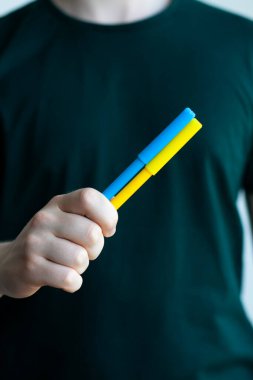 Rusya ile savaşta Ukrayna 'ya destek. Genç bir adam Ukrayna bayrağının bir sembolü olarak sarı ve mavi keçeli kalemler tutuyor. Kavramsal fotoğraf.