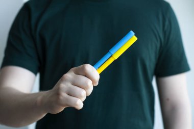 Rusya ile savaşta Ukrayna 'ya destek. Genç bir adam Ukrayna bayrağının bir sembolü olarak sarı ve mavi keçeli kalemler tutuyor. Kavramsal fotoğraf.