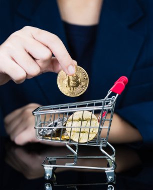 İş kadını, alışveriş arabasında altın Bitcoin simgesi tutuyor. Bitcoin popüler kripto para birimlerinden biri.