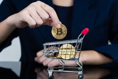İş kadını, alışveriş arabasında altın Bitcoin simgesi tutuyor. Bitcoin popüler kripto para birimlerinden biri.