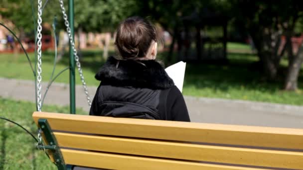读一书在秋天公园的长凳上的女孩 — 图库视频影像