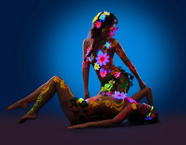 Mulheres nuas com brilho uv corpo arte e flores — Fotografia de Stock