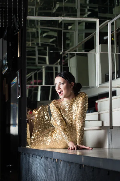 Beauty woman in gold dress posing on bar table — Stock Photo, Image