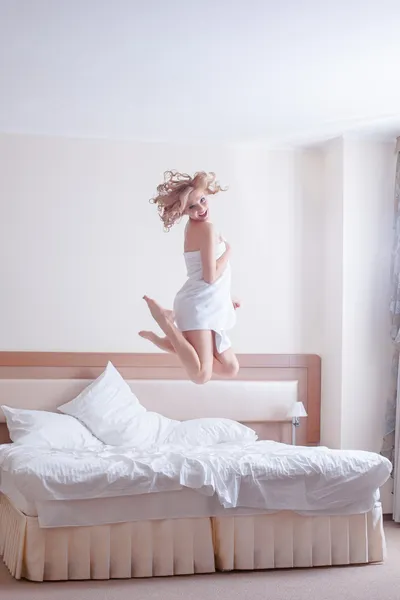 Glad ung kvinna hoppar på sängen — Stockfoto
