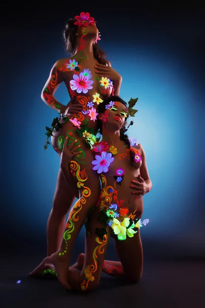 Pareja de mujeres con brillo uv cuerpo arte y flores —  Fotos de Stock