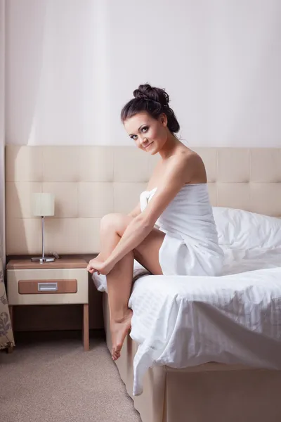 Улыбающаяся брюнетка сидит на кровати отеля — стоковое фото