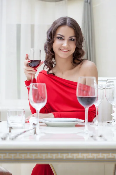 Usmívající se bruneta v červených šatech sedí u stolu — Stock fotografie