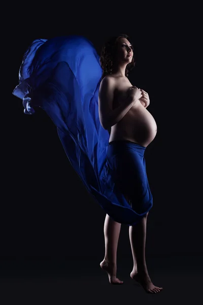 Mujer embarazada conmovedora posando en tela azul — Foto de Stock