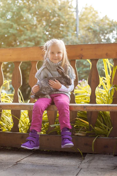 Smiling little girl posing in arbor with rabbit — Stock Photo, Image