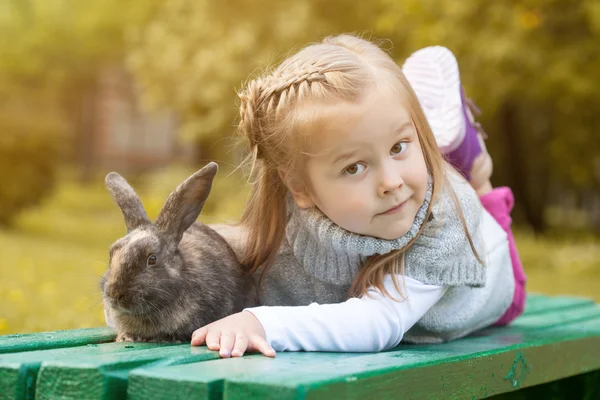 Roztomilý hnědooká holka leží na lavici s králíčkem — Stock fotografie