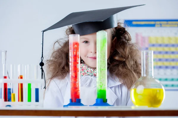 Lustiges kleines Mädchen schaut aus bunten Fläschchen — Stockfoto