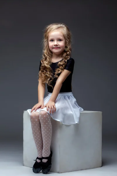 Smiling cute girl posing sitting on cube in studio — Stock Photo, Image