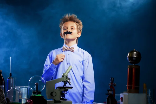 Симпатичный школьник позирует с фальшивыми усами в лаборатории. — стоковое фото