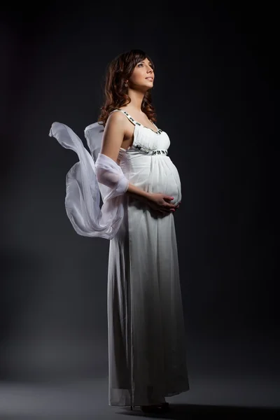 Mulher grávida sonhadora posando em vestido branco longo Imagem De Stock