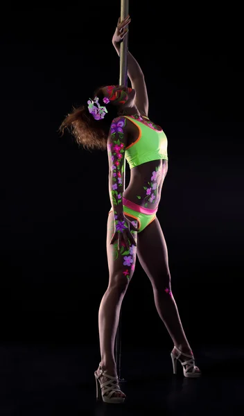 Грациозная танцовщица с неоновым макияжем, позирующая рядом с пилоном — стоковое фото