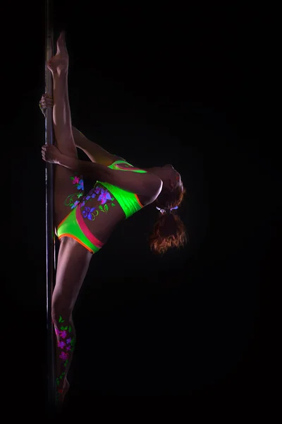 Гибкая девушка танцует на шесте под ультрафиолетовым светом — стоковое фото