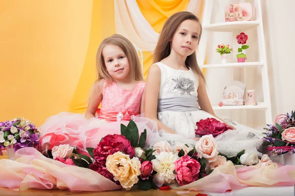 Pretty twins posing with flowers in studio — Stock Photo, Image