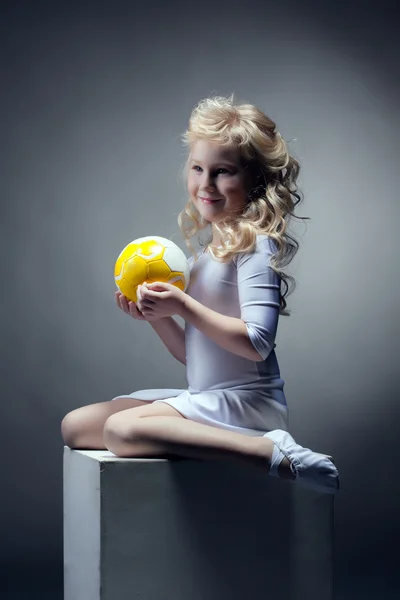 Söt blond gymnast poserar med boll på kub — Stockfoto