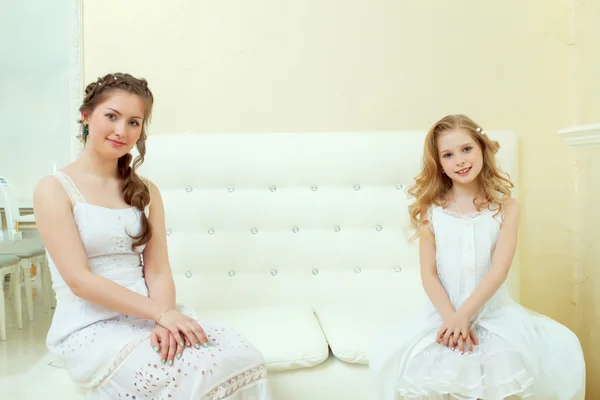 Lovely elegant sisters sitting on white couch — Stock Photo, Image
