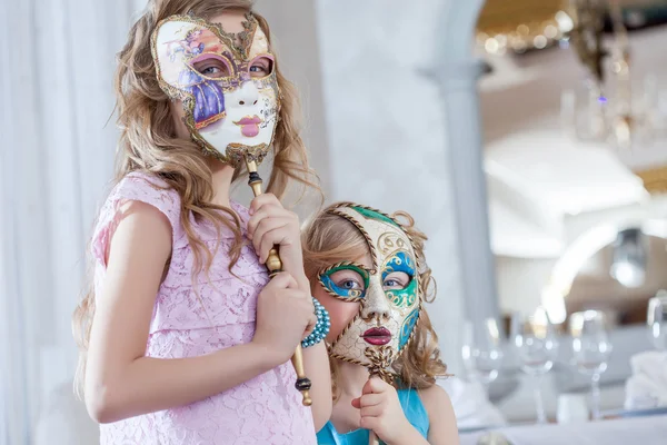 Irmãs bonitos posando rostos escondidos atrás de máscaras — Fotografia de Stock