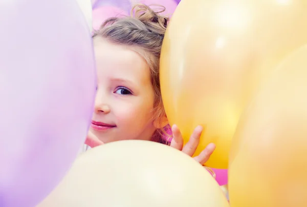 Cute little girl peeking out from behind balloons — Stock Photo, Image