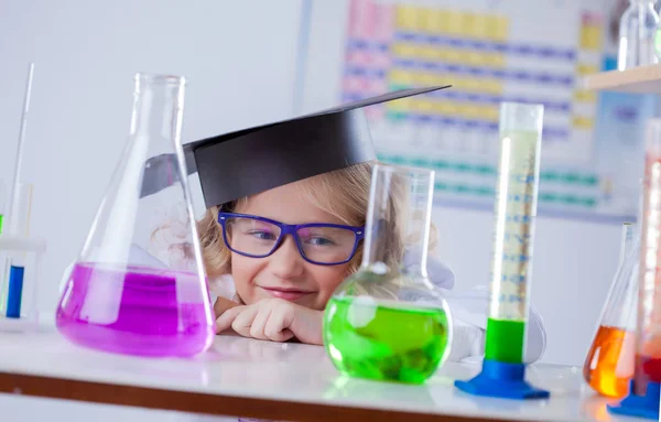 Funny little blonde looks on flasks with reagents — Stock Photo, Image