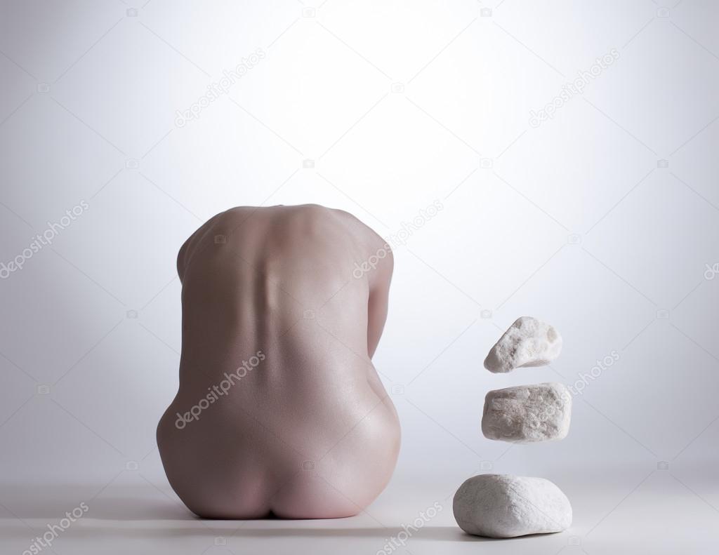 Rear view of nude girl mentally commands stones
