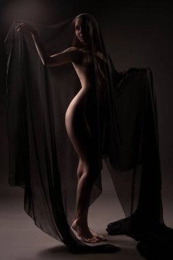 Şehvetli çıplak kadın modeli karanlıkta dikiliyor ve başka tarafa bakıyor.