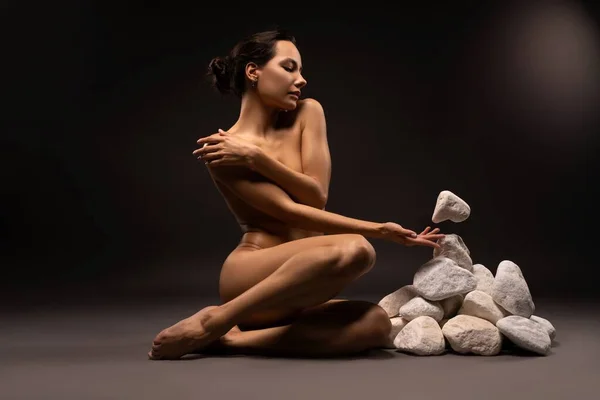 Naked slim woman near heap of levitating stones in studio — Stockfoto