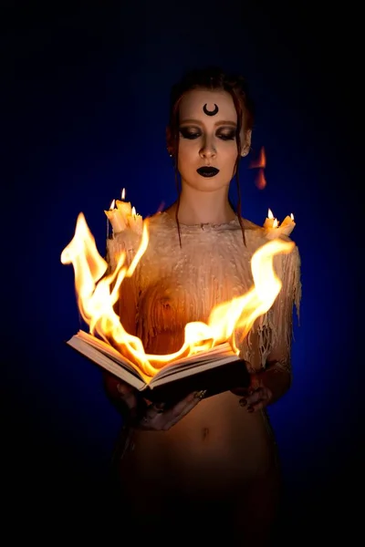 Seductive witch with burning book on black background