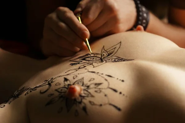 Художник делает татуировку хны на груди голой женщины — стоковое фото