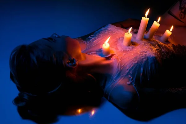 Nude woman with candles on body in dark studio