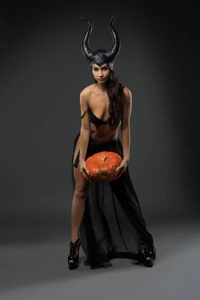 Sexy witch in black Halloween costume with pumpkin
