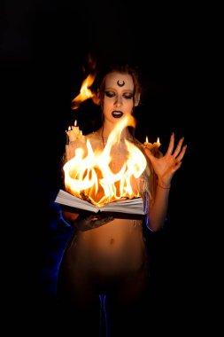 Cadı makyajlı ve omuzlarında mumlarla yanan büyü kitabına bakan bir kadın. Sihirli bir kavram.