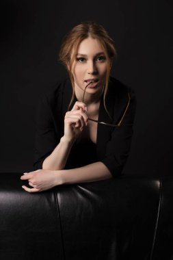 çıplak iş - şık kızıl saçlı iş kadını gözlüklü siyah kanepenin yanında çıplak göğüs üzerinde poz veriyor