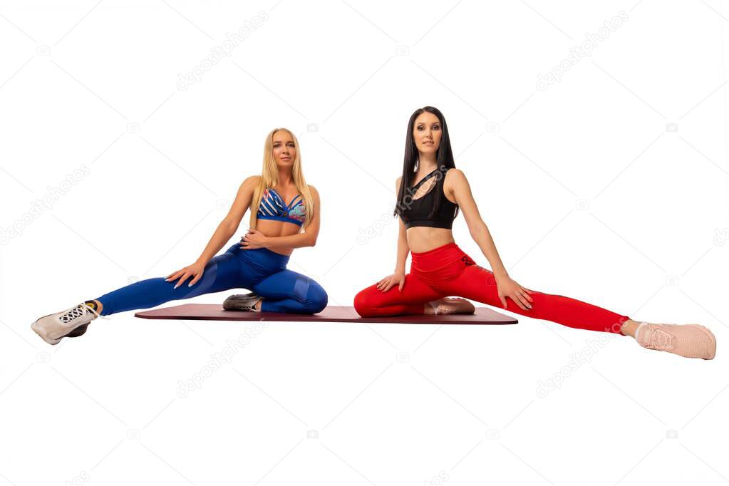 Full body of motivated young female athletes with long blond and dark hair in sportswear sitting on mat while training together against white background - wide angle view
