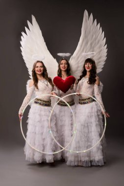 Beyaz elbiseli, şapkalı, gri arka planda kameraya bakan mutlu genç bir kadın.